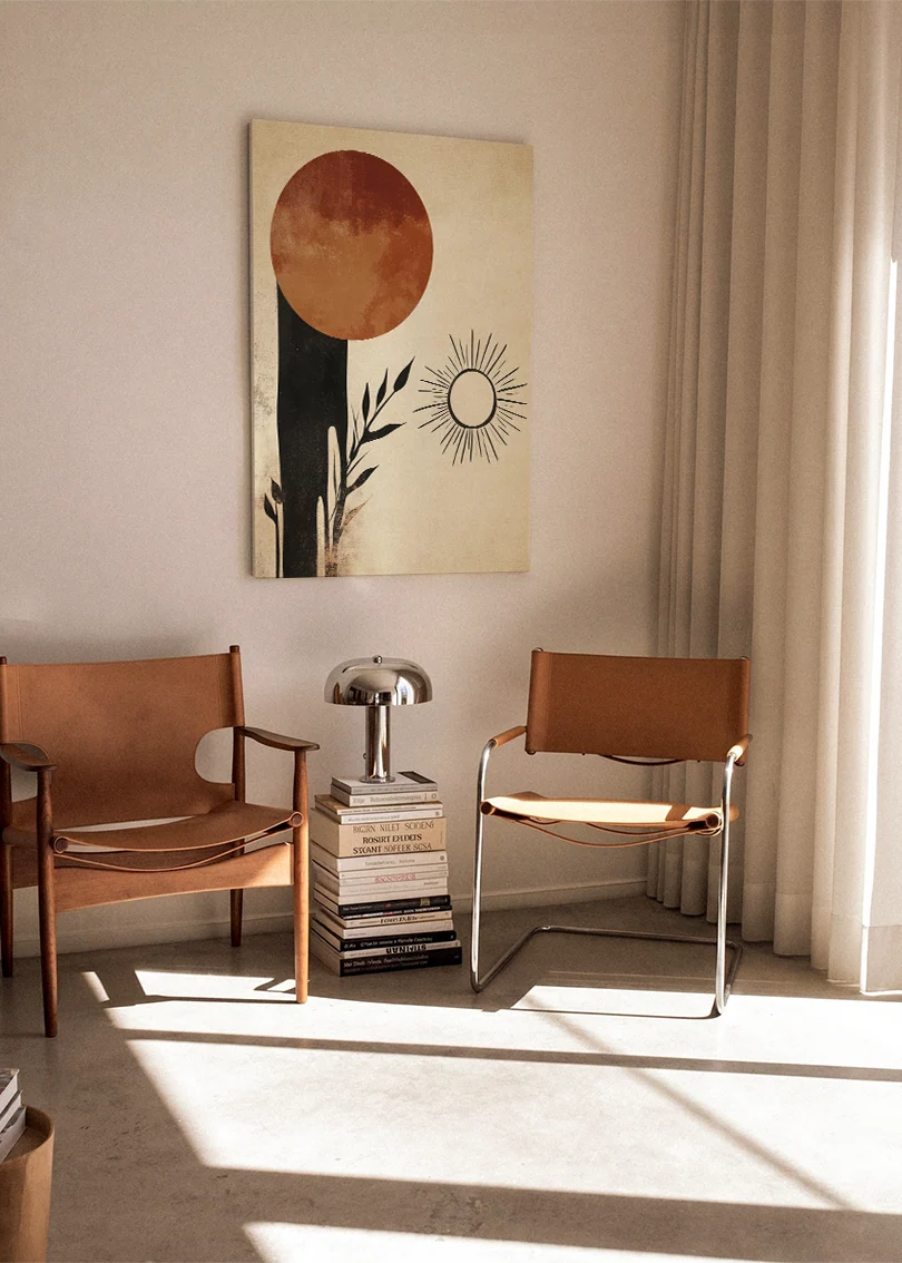 Akustikbillede med en terrakottacirkel med en lille sol og sorte former, ophængt over en brun lænestol i et lyst rum