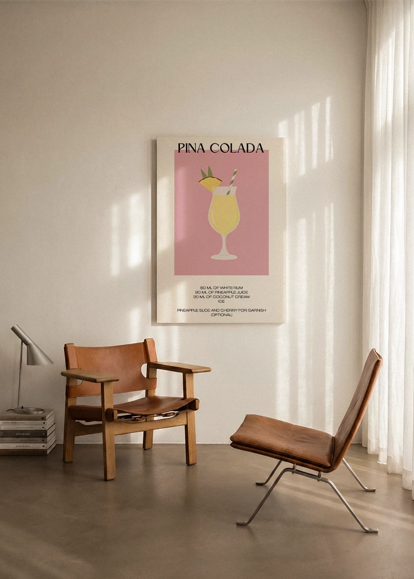 Akustikbillede med en minimalistisk cocktailplakat med Pina Colada, ophængt over en lænestol ved gardinet