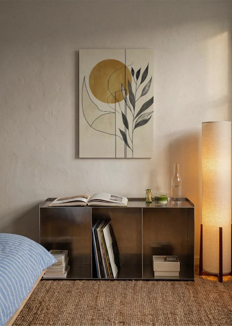 Akustikbillede med en gylden cirkel med grene i beige, over sengegavlen i et soveværelse med tændt lampe