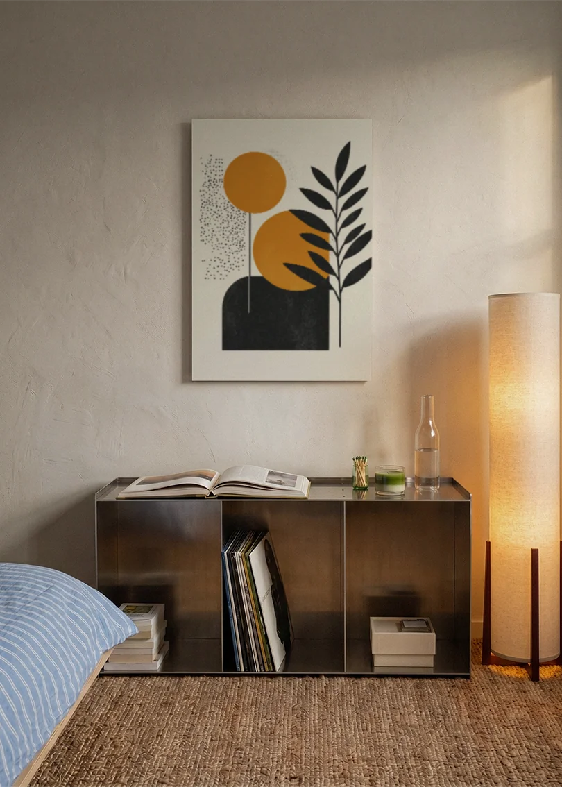 Akustikbillede med orange cirkler med et sort blad, over sengegavlen i et soveværelse med tændt lampe