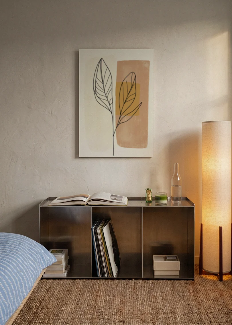 Akustikbillede med et gyldent blad på et terrakottafarvet felt, over sengegavlen i et soveværelse med tændt lampe