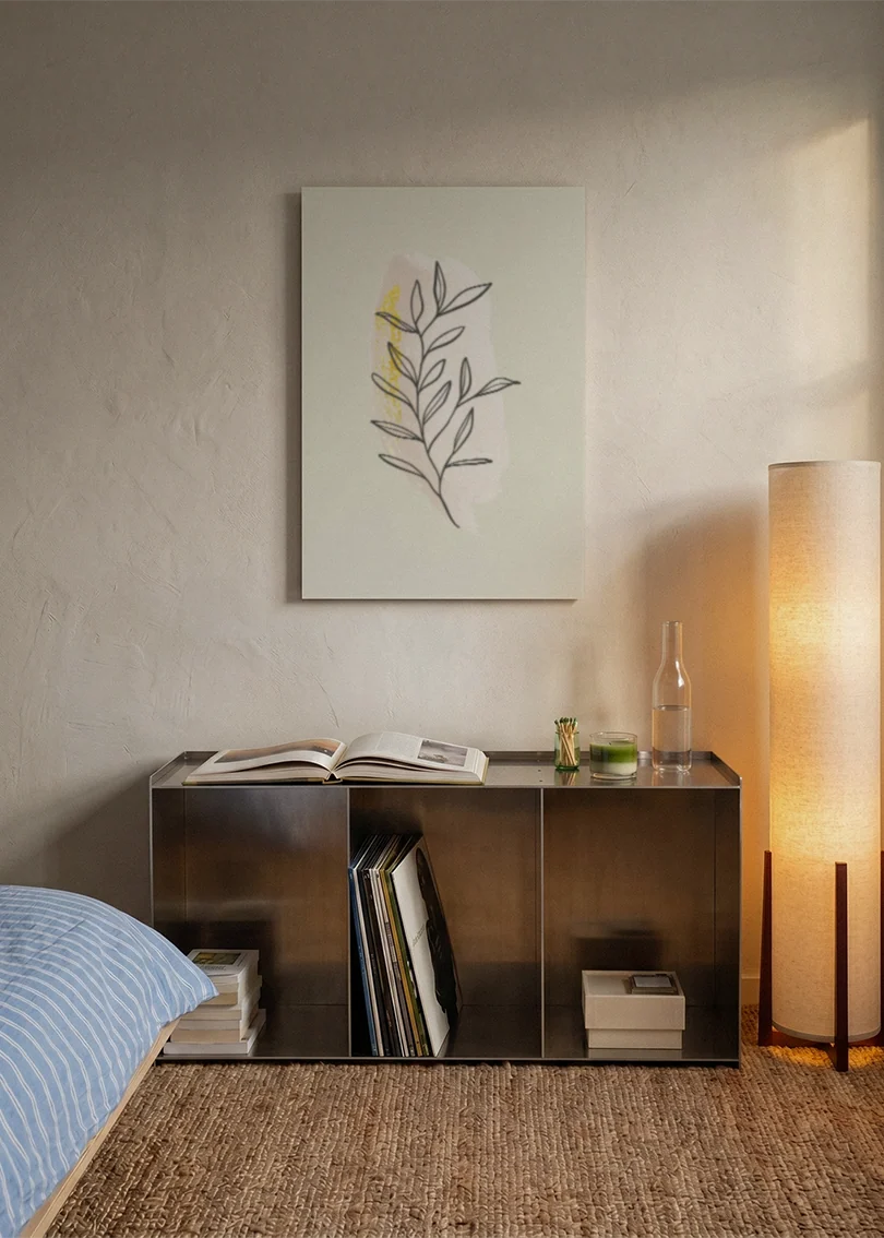 Akustikbillede med en gul gren med tegnede blade, over sengegavlen i et soveværelse med tændt lampe