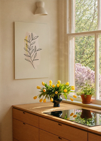 Akustikbillede med en gul gren med tegnede blade, ved et vindue med en blomsterbuket i karmen