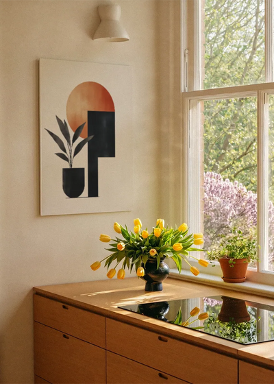Akustikbillede med en terrakottacirkel med sorte og blå geometriske former, ved et vindue med en blomsterbuket i karmen