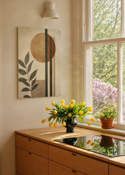 Akustikbillede med en beige cirkel bag grønne blade, ved et vindue med en blomsterbuket i karmen