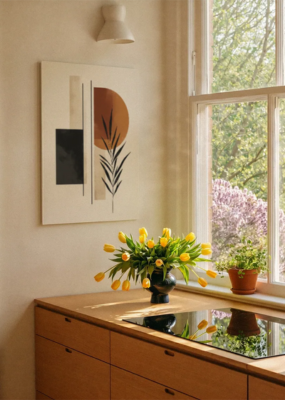 Akustikbillede med sorte og beige felter med et grønt blad, ved et vindue med en blomsterbuket i karmen