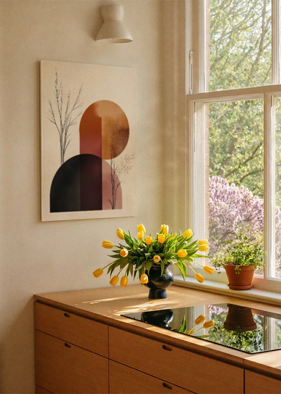 Akustikbillede med sorte og terrakottafarvede former med lyserøde cirkler, ved et vindue med en blomsterbuket i karmen