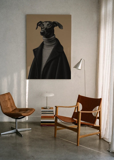 Akustikbillede med en whippet i sort rullekrave, ophængt over en lænestol ved gardinet med gulvlampe