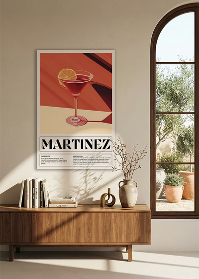 Akustikbillede med en retro cocktailplakat med Martinez, over en skænk i valnød ved et buet vindue