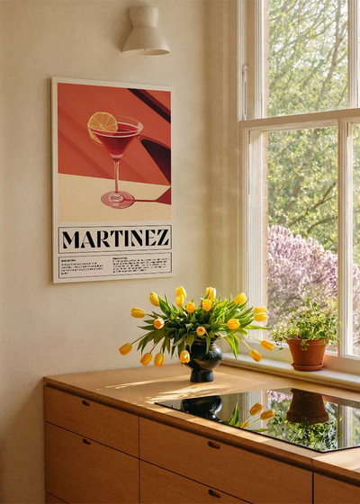 Akustikbillede med en retro cocktailplakat med Martinez, ved et køkkenvindue med gule tulipaner