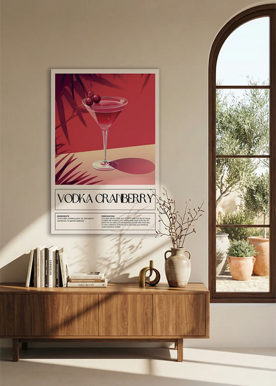 Akustikbillede med en retro cocktailplakat med Vodka Cranberry, over en skænk i valnød ved et buet vindue