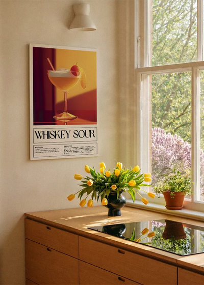 Akustikbillede med en retro cocktailplakat med Whiskey Sour, ved et køkkenvindue med gule tulipaner