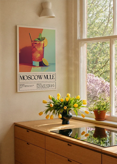 Akustikbillede med en retro cocktailplakat med Moscow Mule, ved et køkkenvindue med gule tulipaner