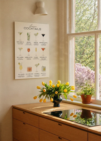 Akustikbillede med en oversigtsplakat med klassiske cocktails, ved et køkkenvindue med gule tulipaner