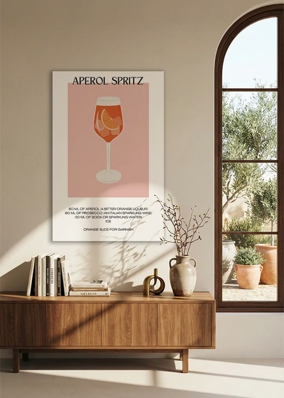 Akustikbillede med en minimalistisk cocktailplakat med Aperol Spritz, over en skænk i valnød ved et buet vindue