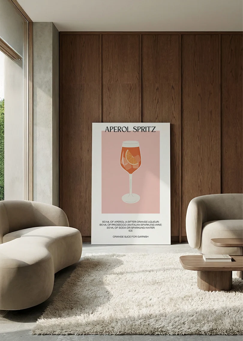 Akustikbillede med en minimalistisk cocktailplakat med Aperol Spritz, lænet mod vægpanel i valnød ved sofaen