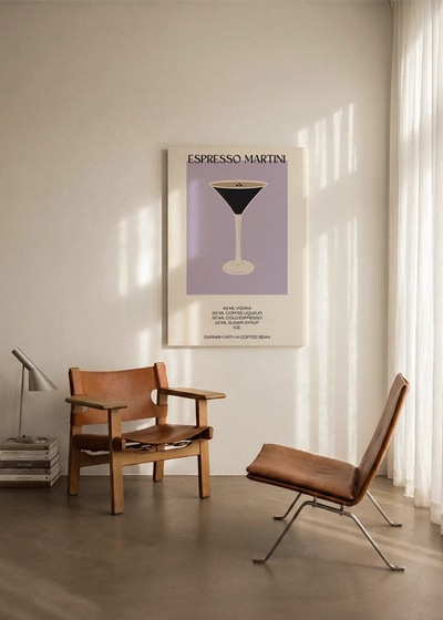 Akustikbillede med en minimalistisk cocktailplakat med Espresso Martini, ophængt over en lænestol ved gardinet