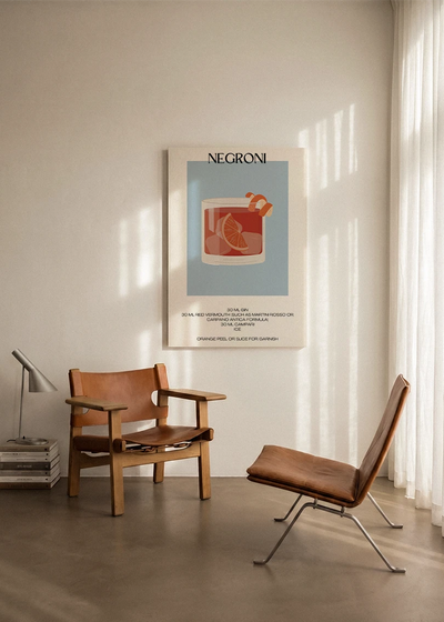 Akustikbillede med en minimalistisk cocktailplakat med Negroni, ophængt over en lænestol ved gardinet