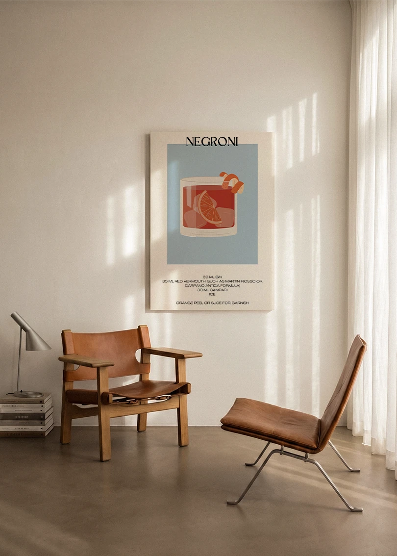Akustikbillede med en minimalistisk cocktailplakat med Negroni, ophængt over en lænestol ved gardinet