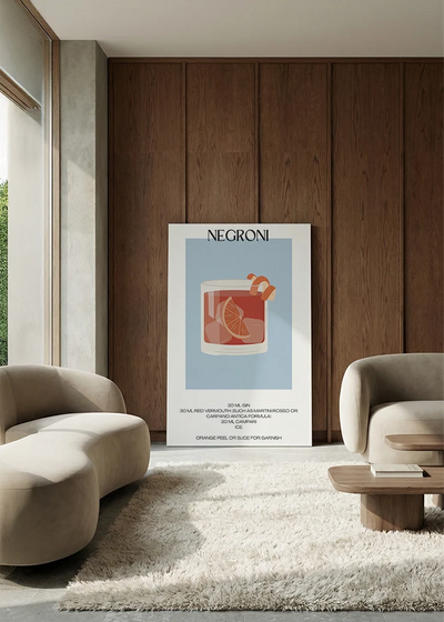 Akustikbillede med en minimalistisk cocktailplakat med Negroni, i en lounge med bugtet sofa mod vægpanel i valnød