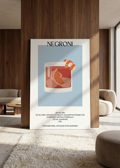 Akustikbillede med en minimalistisk cocktailplakat med Negroni, lænet mod vægpanel i valnød ved sofaen