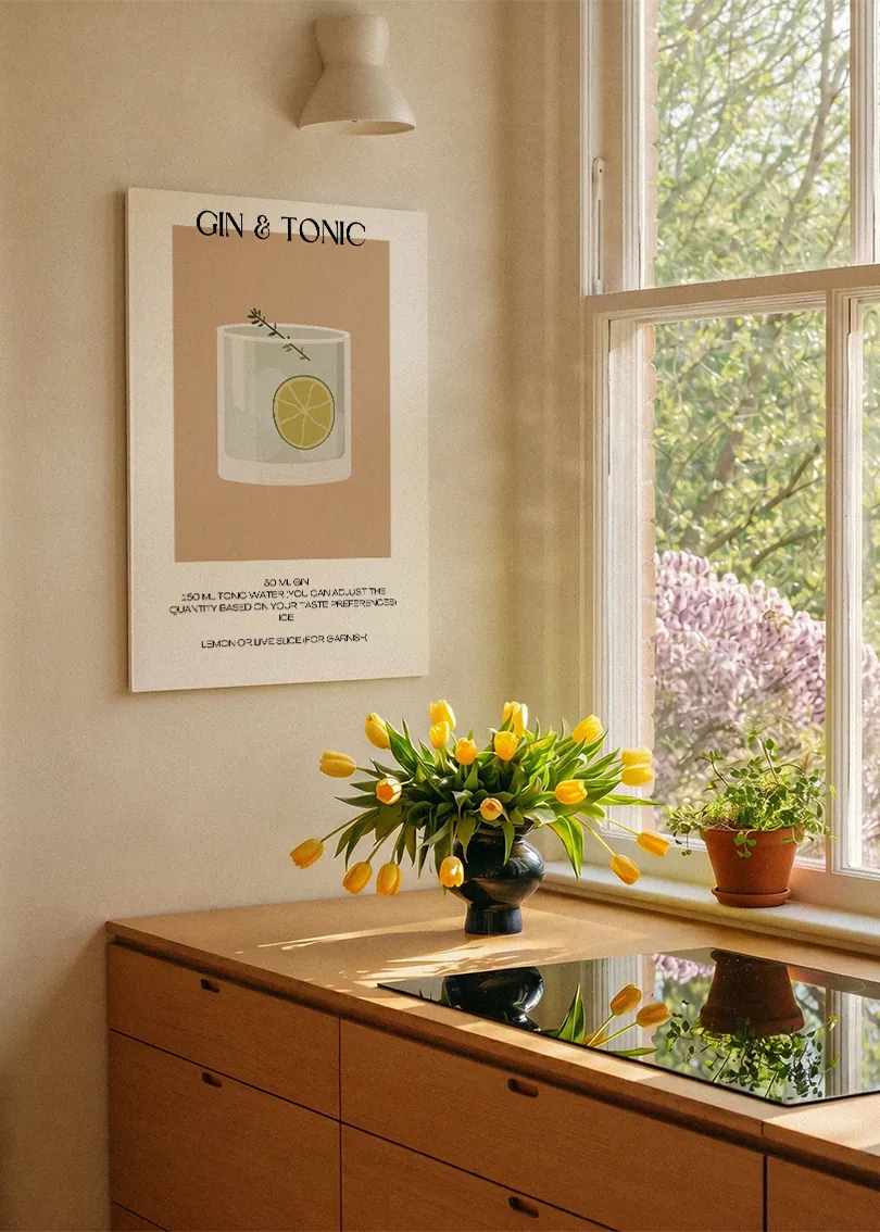 Akustikbillede med en minimalistisk cocktailplakat med Gin & Tonic, ved et køkkenvindue med gule tulipaner
