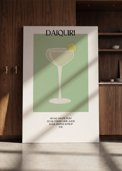 Akustikbillede med en minimalistisk cocktailplakat med Daiquiri, lænet mod en skabsvæg i valnød
