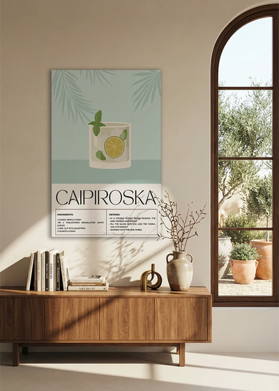 Akustikbillede med en retro cocktailplakat med Caipiroska, over en skænk i valnød ved et buet vindue