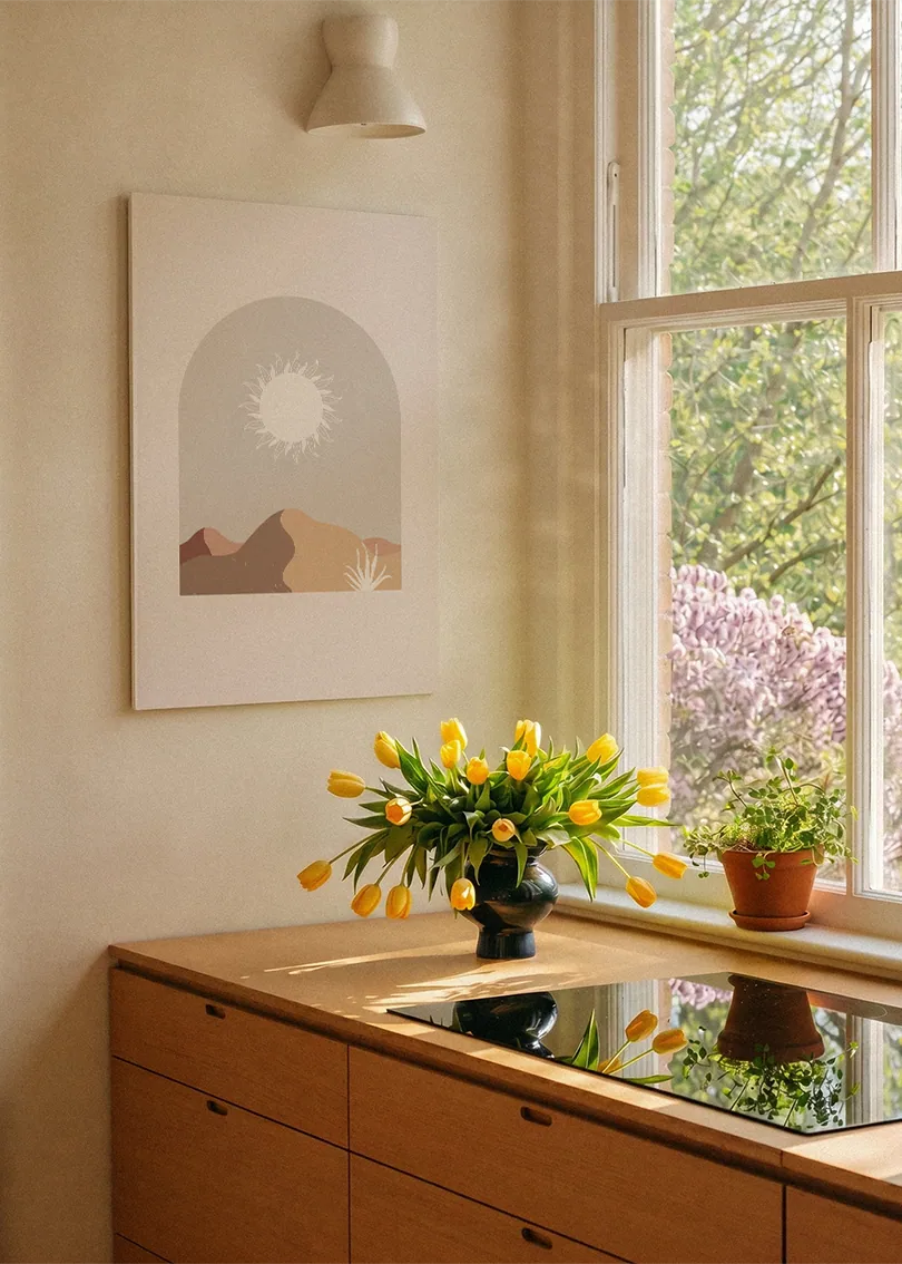 Akustikbillede med en hvid sol over bjerge i beige, ved et vindue over køkkenbordet med gule tulipaner