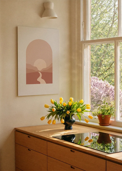 Akustikbillede med en sol over en flod mellem bakker, ved et vindue over køkkenbordet med gule tulipaner