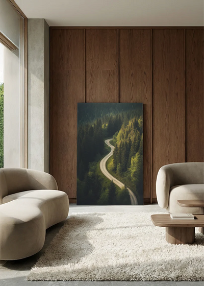 Akustikbillede med dronefoto af en snoet vej gennem tæt grøn nåleskov, i lounge med bugtet sofa mod vægpanel i valnød