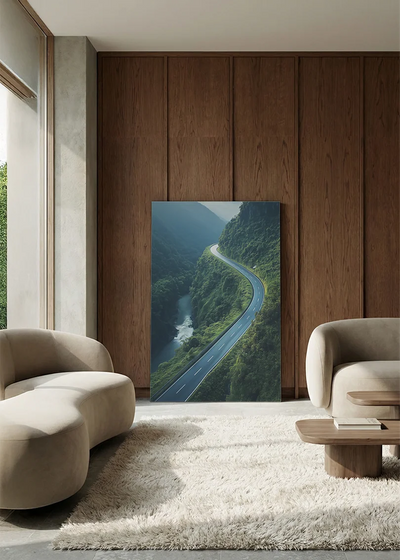 Akustikbillede med dronefoto af en snoet bjergvej langs en flod i en grøn dal, i lounge med bugtet sofa mod vægpanel i valnød