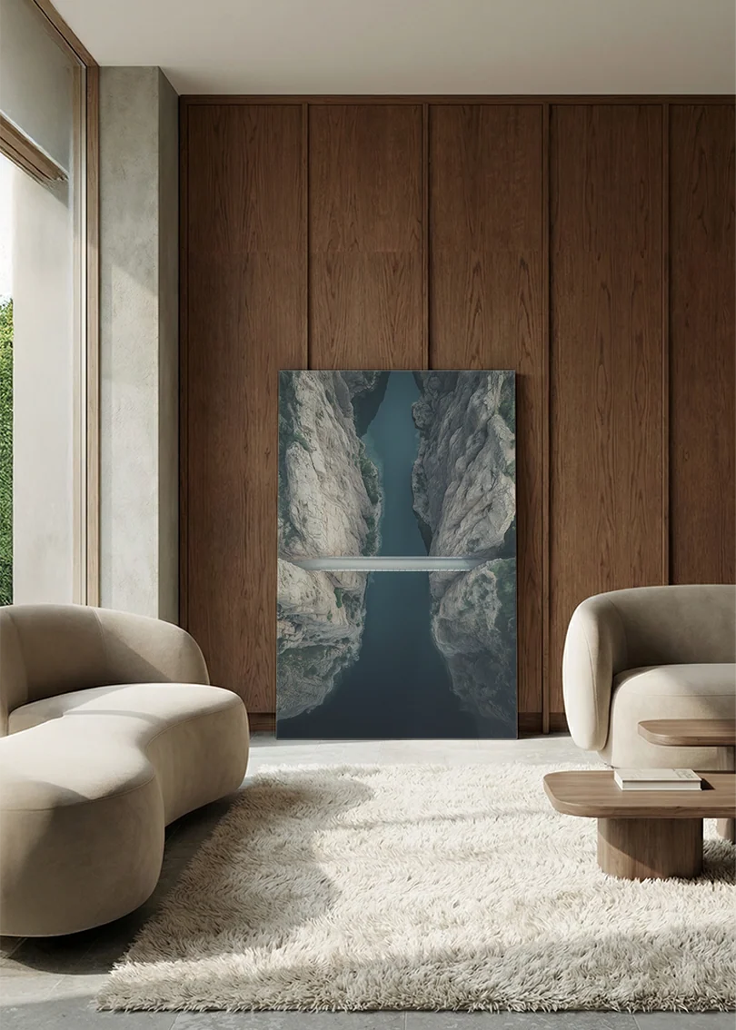 Akustikbillede med dronefoto af en bro over en smal flod i en lys klippekløft, i lounge med bugtet sofa mod vægpanel i valnød