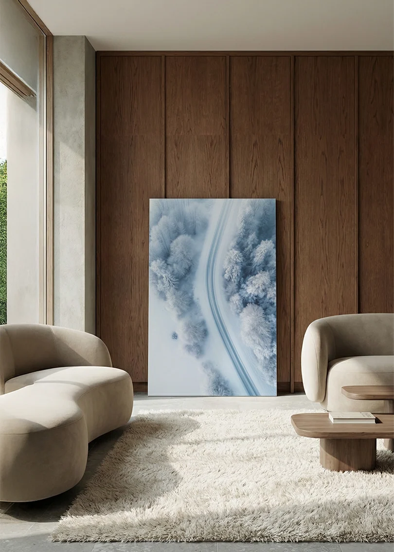 Akustikbillede med dronefoto af en vej gennem sneklædt vinterskov, i lounge med bugtet sofa mod vægpanel i valnød