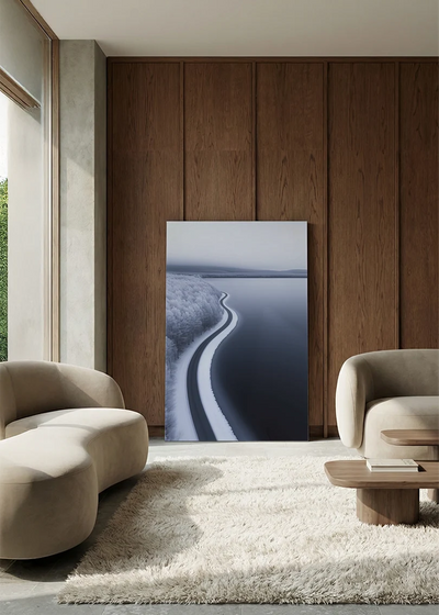 Akustikbillede med dronefoto af en snoet snedækket vej langs en iskold kyst, i lounge med bugtet sofa mod vægpanel i valnød