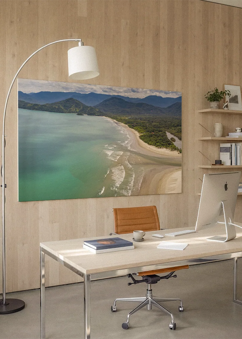 Akustikbillede med kystlinje med turkis hav og en lang sandstrand, på hjemmekontor med hvidt skrivebord og buelampe