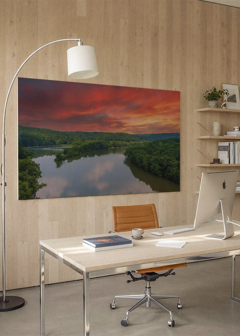 Akustikbillede med en flod ved solnedgang under rød og orange himmel, på hjemmekontor med hvidt skrivebord og buelampe
