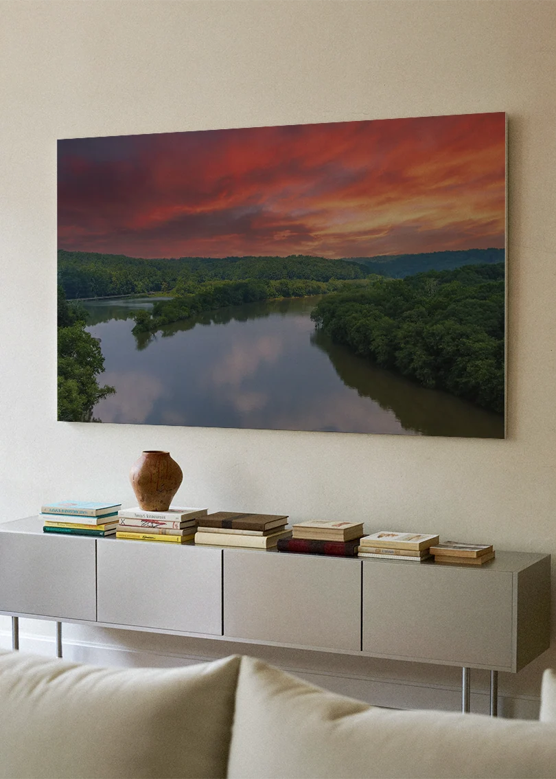 Akustikbillede med en flod ved solnedgang under rød og orange himmel, over hvid skænk med sofa i forgrunden