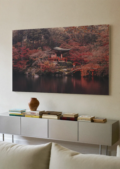 Akustikbillede med et japansk tempel i rød efterårsskov ved vand, over hvid skænk med sofa i forgrunden